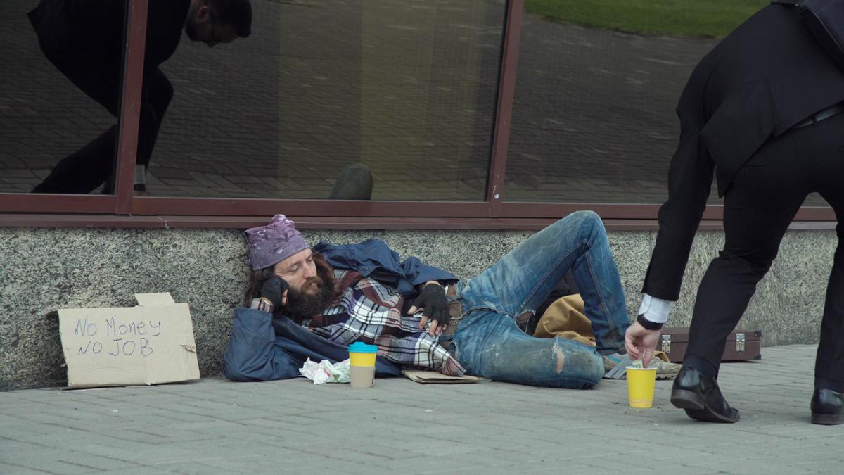 Man laying on side of street with sign that says "no money no job"